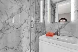A bathroom with a marble wall, a glass shower enclosure, a white sink, and a mirror.