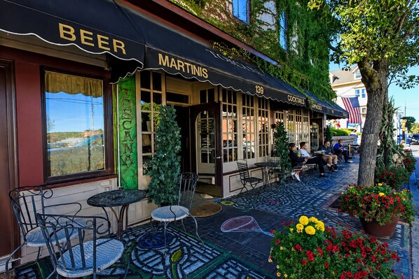 A bar with outdoor seating, a sign reading 'BEER MARTINIS COCKTAILS,' and a view of a residential area.
