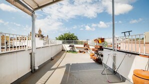Una terraza en la azotea con vistas a un edificio histórico, una valla blanca y plantas en macetas.