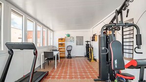 Un gimnasio con cinta de correr, máquinas de pesas y una pequeña mesa con sillas.