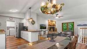 A modern kitchen with white cabinetry, a central island, and a dining area with a glass table and metal chair. - Modern Family Cabin in the Smokies + Mtn Views! (Pigeon Forge)