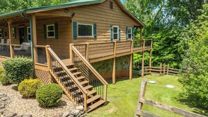 A wooden cabin with a covered porch, a staircase leading to a deck, and a fenced yard. - Modern Family Cabin in the Smokies + Mtn Views! (Pigeon Forge)