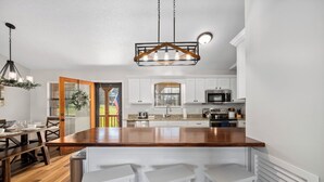 A modern kitchen with white cabinetry, a wooden island, and a hanging light fixture. - Modern Family Cabin in the Smokies + Mtn Views! (Pigeon Forge)