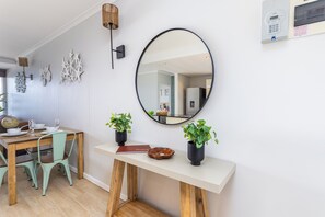 A dining area with a wooden table, green chairs, a white console table with potted plants, a round mirror, and wall-mounted decor. - Blu Horizon
Modern Beachfront 3BR with Epic Table Mountain Views (Cape Town)