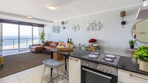 Een moderne keuken met een groot eiland, een eethoek met uitzicht en een woonruimte met een bank en een plant.