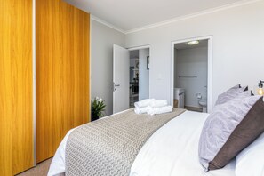 A hotel room with a bed, a wooden wardrobe, and an open door leading to a bathroom. - Blu Horizon
Modern Beachfront 3BR with Epic Table Mountain Views (Cape Town)