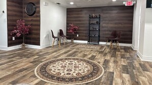 Una zona d'entrada amb terra de fusta, dues cadires, un moqueta rodona, un rellotge i una estant amb elements decoratius.