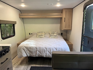 A compact bedroom with a bed, two pillows, a small dresser, and a window.
