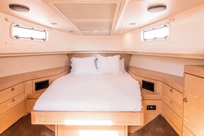 Ein kleines, helles Schlafzimmer mit einem Einzelbett, eingebauten Schubladen und zwei kleinen Fenstern.