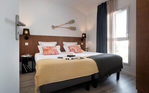 A neatly arranged hotel room with a bed, bedside tables, a wall-mounted lamp, and a window with curtains. - Picturesque 6-person Duplex Oasis (Les Sables-d'Olonne)