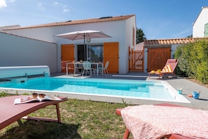 Una piscina con sillones de descanso y una mesa con sombrilla.