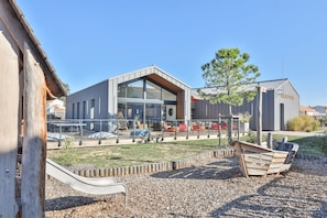 A modern building with a glass facade, outdoor seating, and a playground area. - Picturesque 6-person Duplex Oasis (Les Sables-d'Olonne)