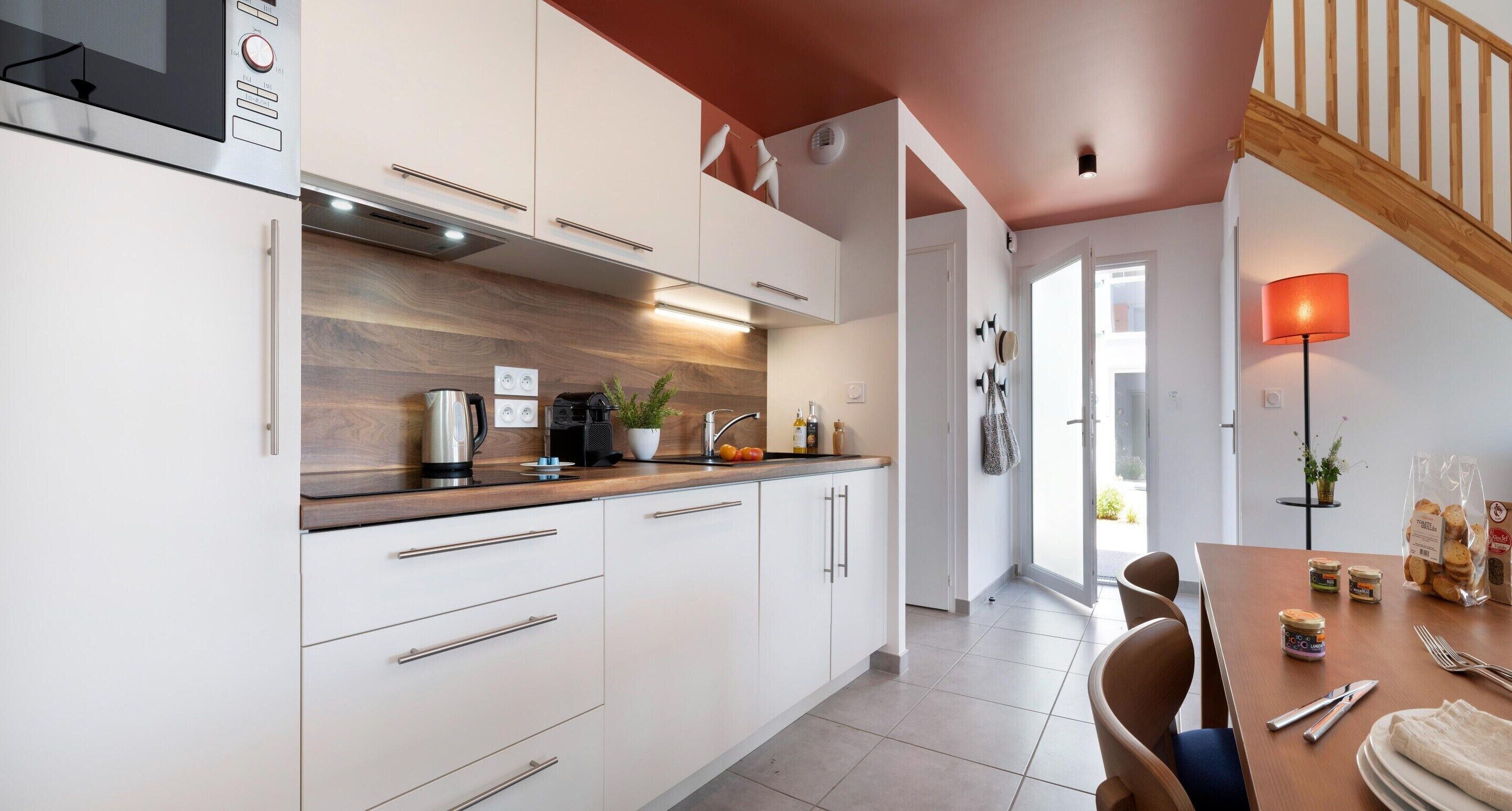 A modern kitchen with white cabinets, a wooden countertop, and a dining area with a table and chairs.