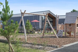 A playground with swings and a slide, surrounded by a wooden fence and mulch. - Picturesque 6-person Duplex Oasis (Les Sables-d'Olonne)