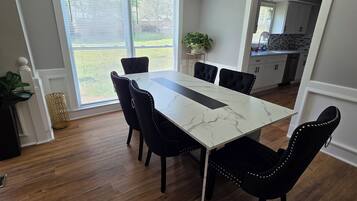 A dining room with a marble table, black upholstered chairs, a chandelier, and a view of the outdoors through large windows.