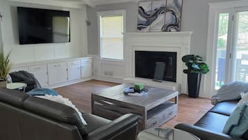 A living room with a fireplace, a ceiling fan, and a large TV.