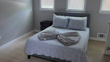 A bedroom with a bed, two bedside tables, and two windows with blinds.