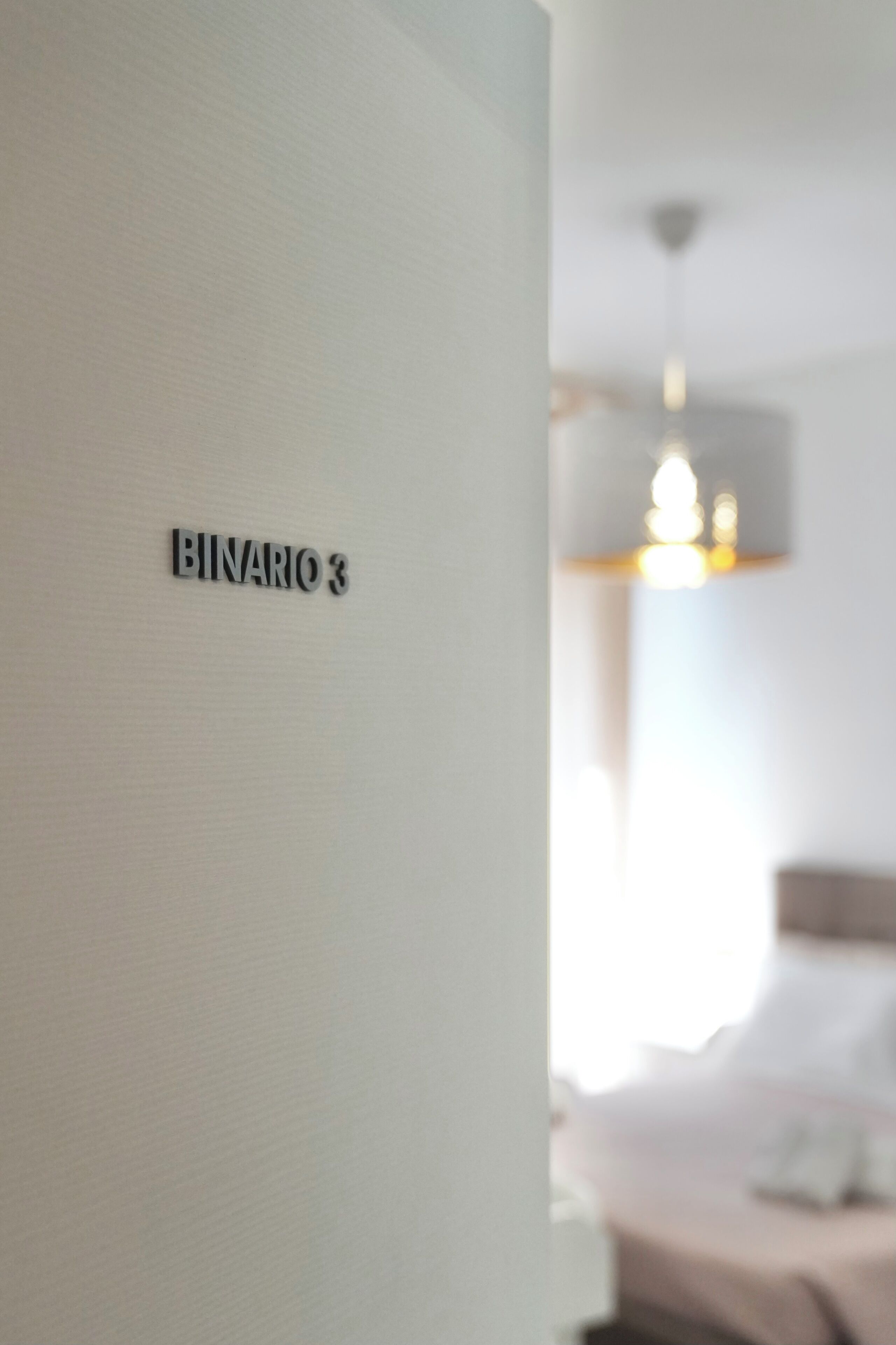 Ein Zimmer mit einer Wandtafel, auf der 'BINARO 3' steht, einem Bett und einer Hängelampe.