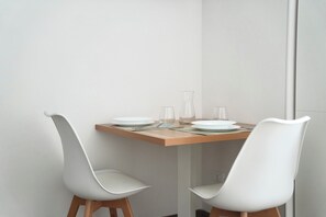 A dining table with four white chairs, a wooden table top, and a white wall. - Termoli Station (Termoli)