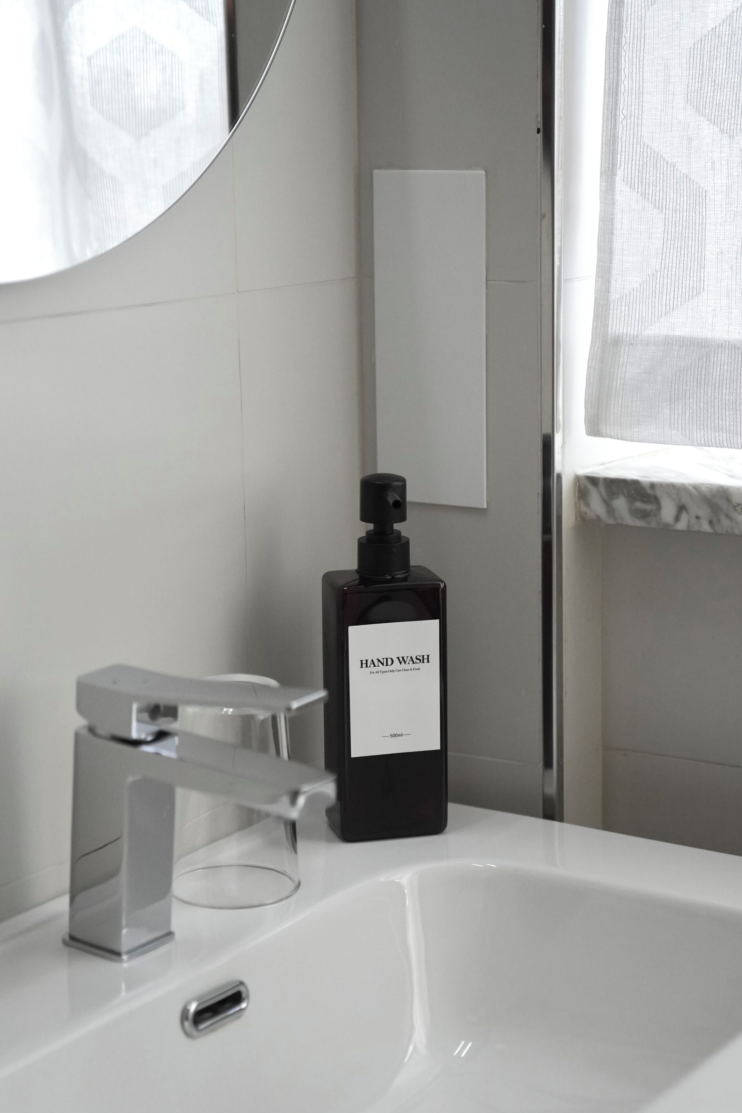 Un baño moderno con un lavabo blanco, un dispensador de jabón negro y un vaso de vidrio transparente.