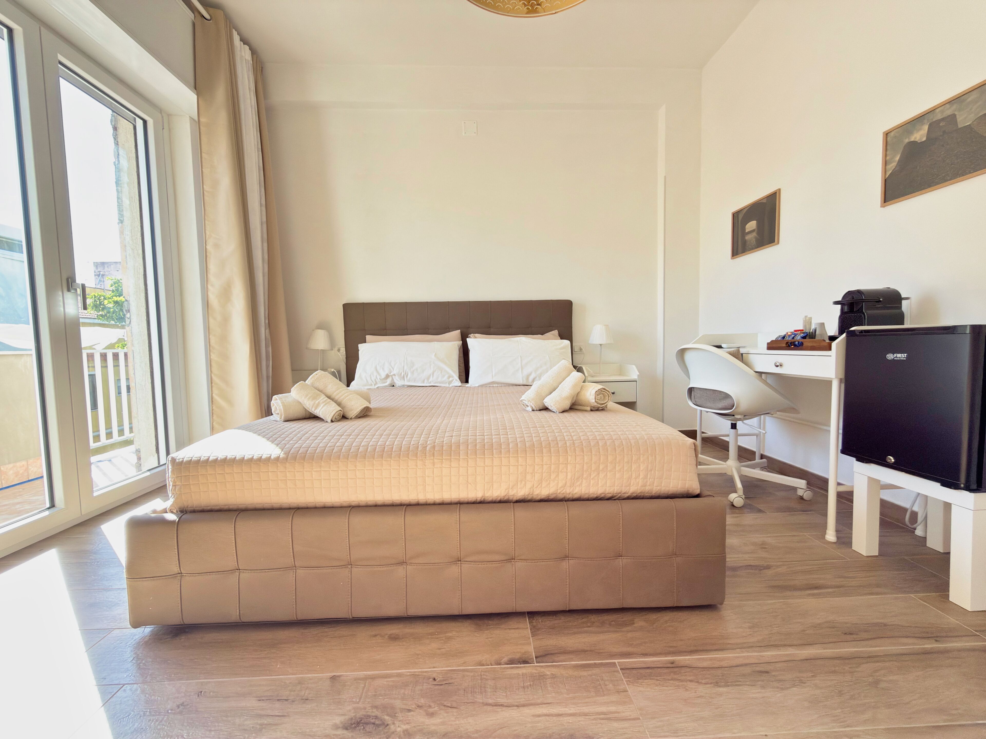 A hotel room with a large bed, a desk, a chair, a TV, and a balcony view.