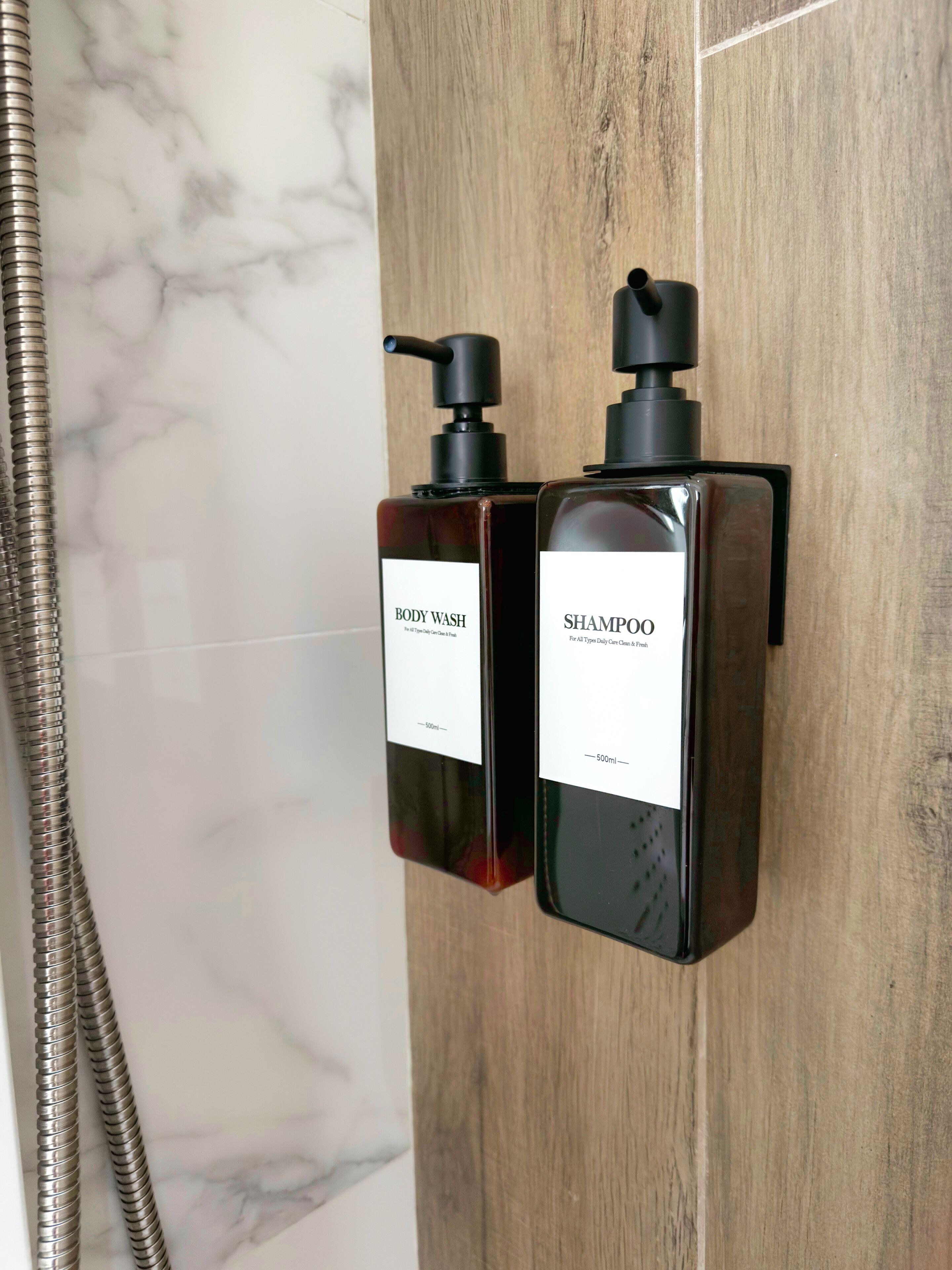 To flasker med body wash og shampoo hænger på en trævæg i et badeværelse.