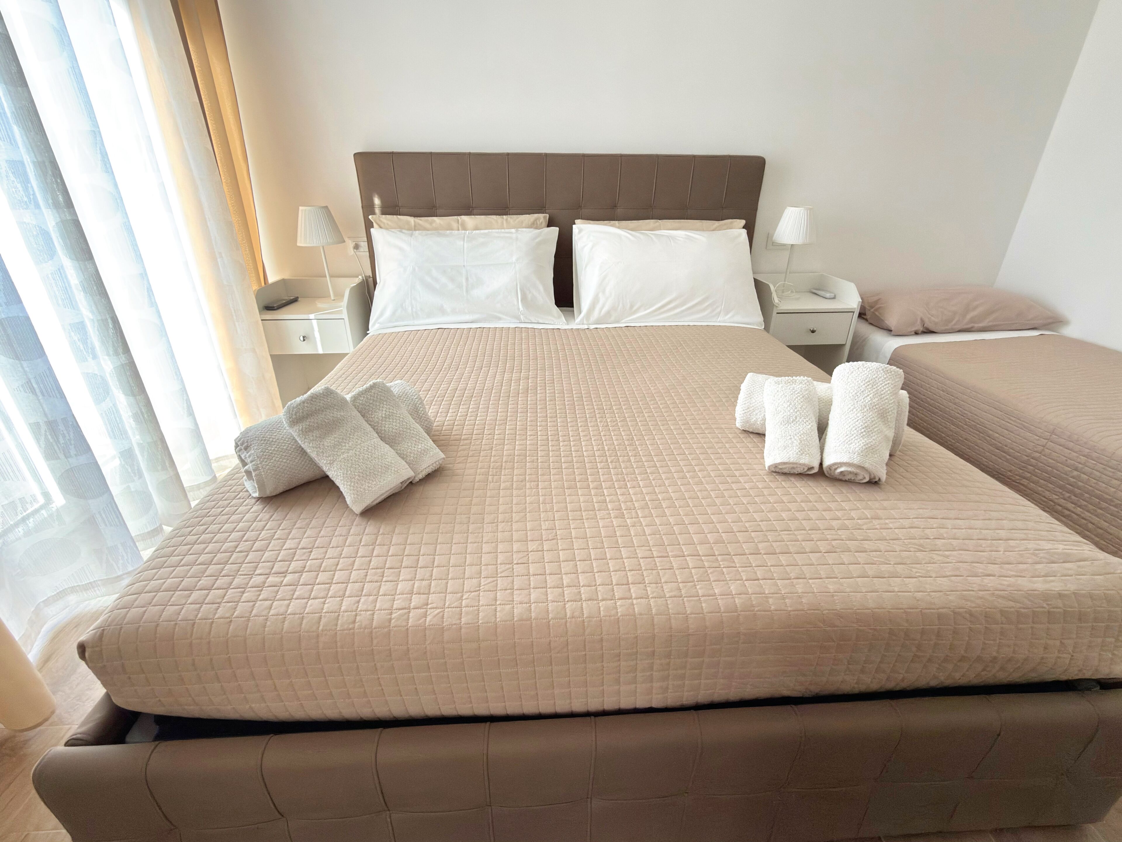 A hotel room with a large bed, two bedside tables, and a window with curtains.