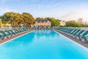 En rektangulär swimmingpool med gröna solstolar längs sidorna, omgiven av ett vitt staket.