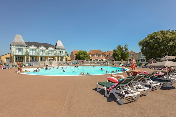 A swimming pool with lounge chairs and a building with a distinctive architectural style. - Holiday House Near Lake & Sea (Talmont-Saint-Hilaire)