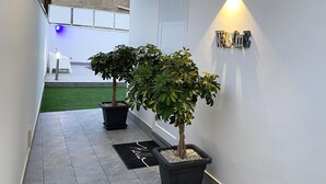 Un couloir agrémenté de plantes en pot, d’un paillasson et d’un luminaire fixé au mur.