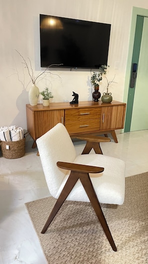 Ein modernes Wohnzimmer mit einem weißen Sofa, einem Holzkasten und einem an der Wand montierten Flachbildfernseher.