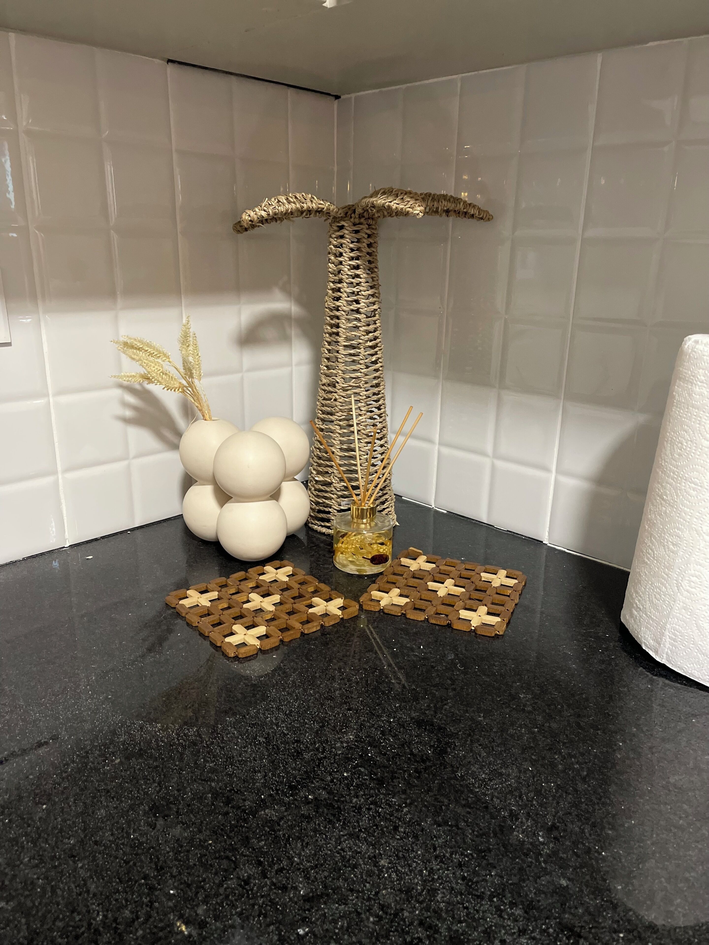 Une pièce avec un comptoir noir, un arbre à chat en fibres tressées, un vase contenant des objets sphériques blancs et un rouleau d’essuie-tout.