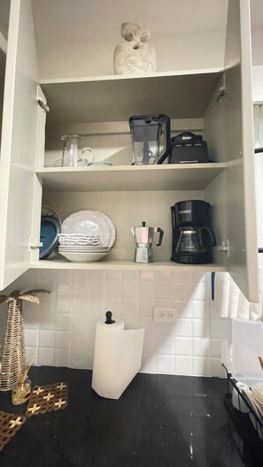 Et køkken med hvide skabe, en kaffemaskine, en blender og en pynteting på hylden.