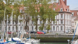 A marina with boats docked, a building with a red roof, and trees in the foreground. - Picturesque Deauville Apartment for 6 (Deauville)