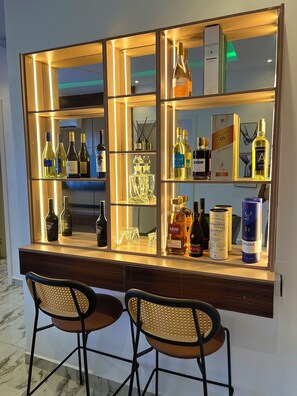 Zona bar con numerosi scaffali pieni di bottiglie di liquore e bicchieri, due sgabelli da bar e uno specchio che riflette l'interno.