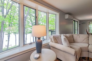 A living room with a sofa, a lamp, and large windows with a view of trees.