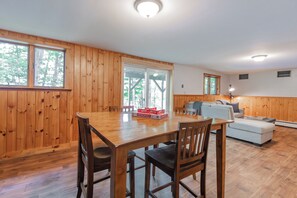 A wooden interior with a dining table, chairs, a sofa, and a window.