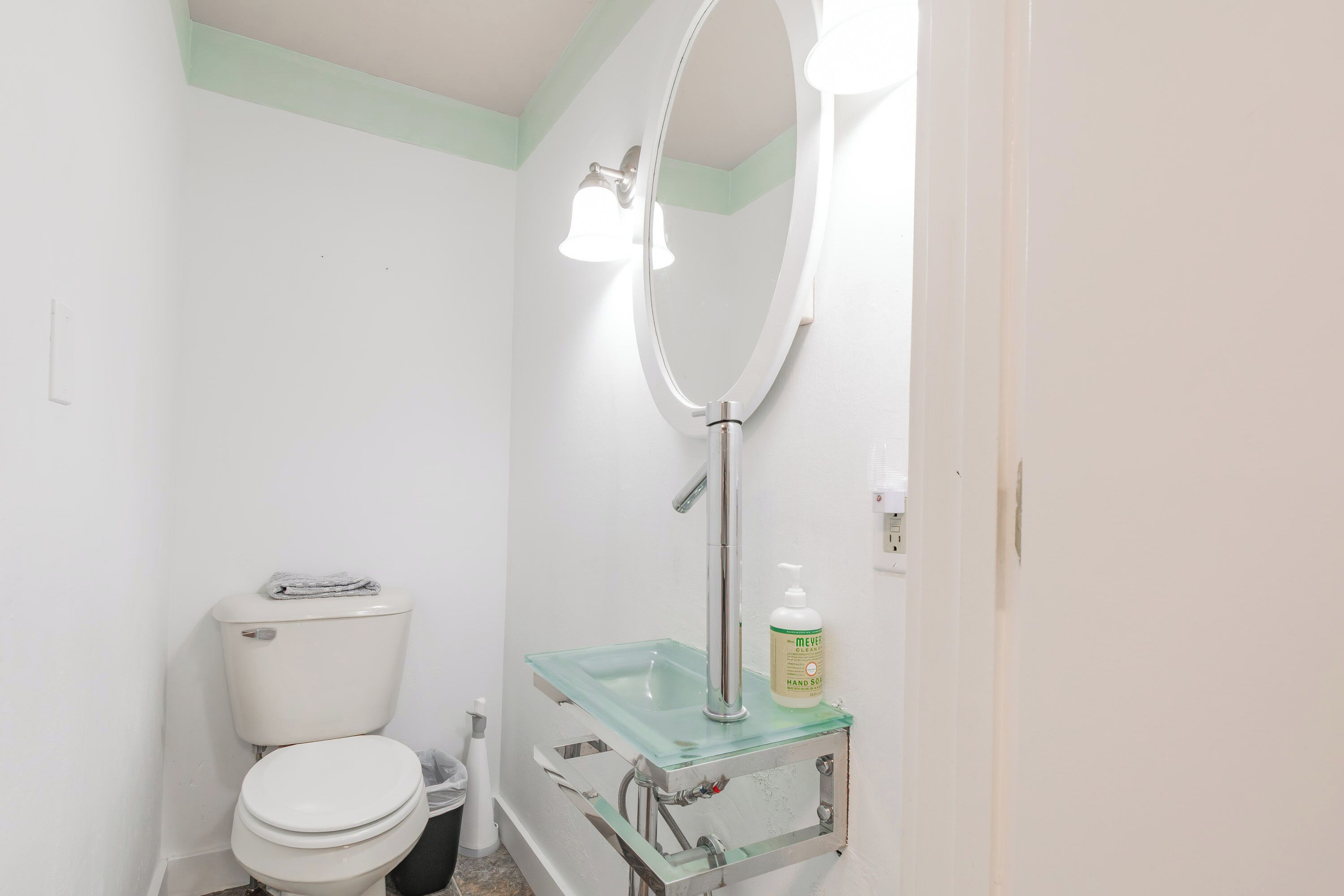Ein Badezimmer mit Toilette, einem Glaswaschbecken mit Seifenspender und einem beleuchteten Spiegel.