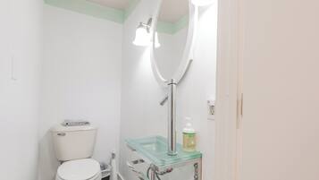 Ein Badezimmer mit Toilette, einem Glaswaschbecken mit Seifenspender und einem beleuchteten Spiegel.