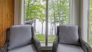 Quarto com duas cadeiras de vime voltadas para uma janela grande com vista para árvores e um cais.
