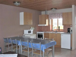 Uma cozinha com armários de madeira, micro-ondas, fogão, pia e uma área de jantar com mesa e cadeiras.