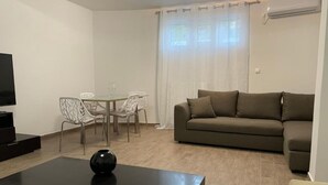 Uma sala de estar com sofá, mesa de centro, televisão e um espaço de jantar com cadeiras.