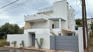 Uma casa moderna de dois andares, com portão cinzento, varanda e escadaria que dá acesso ao andar superior.