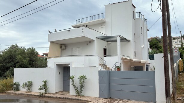 Una casa moderna a due piani con un cancello grigio, un balcone e una scala che conduce al piano superiore.