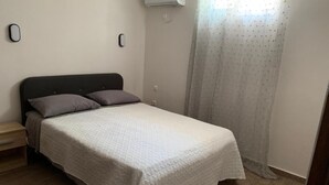 Una camera da letto con un letto, un comodino, un condizionatore d'aria a parete e una finestra con tenda.