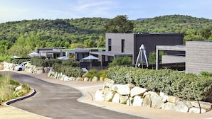 A modern building with a curved driveway, stone landscaping, and a view of a forested hill. - Corsica Haven With Garden (Lecci)