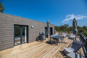 Una terraza moderna al aire libre con piso de madera, una mesa con sillas y dos sombrillas.