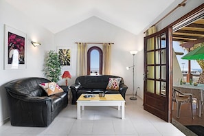 Ein Wohnzimmer mit einer schwarzen Ledersofa, einem weißen Couchtisch, einer Stehlampe und Blick durch ein großes Fenster.