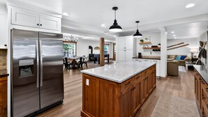 A spacious kitchen with a large island, stainless steel refrigerator, wooden cabinets, and pendant lighting.
