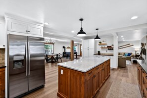 Una cocina amplia con una isla grande, refrigerador de acero inoxidable, armarios de madera e iluminación colgante.